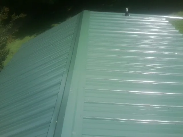 New green metal panels meeting at the ridge of a roof — Flat Roof Repair work by our crew in Howe